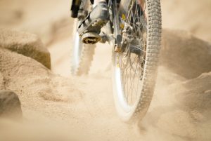 View of the bottom half of a mountain bike as it races down a dusty trail.