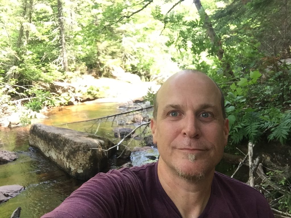 Selfie of a smiling man sitting by a river/