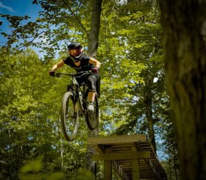 A female mountain biker is riding off a wooden drop on the trail.
